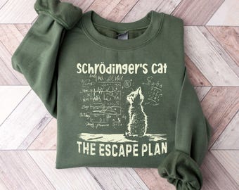 May include: A green sweatshirt with the text "Schrödinger's Cat" above a cat illustration and mathematical equations. Below the cat is the text "The Escape Plan". The sweatshirt has long sleeves and a crew neck.