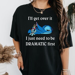May include: Black t-shirt featuring a blue Stitch character from Lilo & Stitch. The text on the shirt reads "I'll get over it I just need to be DRAMATIC first."