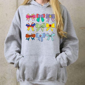 May include: A gray hoodie with a colorful bow design. The bows are in various colors, including pink, blue, yellow, and green.