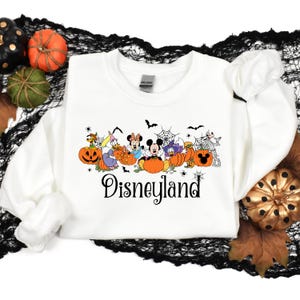 May include: White sweatshirt with a Halloween-themed design featuring Mickey Mouse and friends dressed in costumes and holding pumpkins. The text "Disneyland" is printed below the characters.