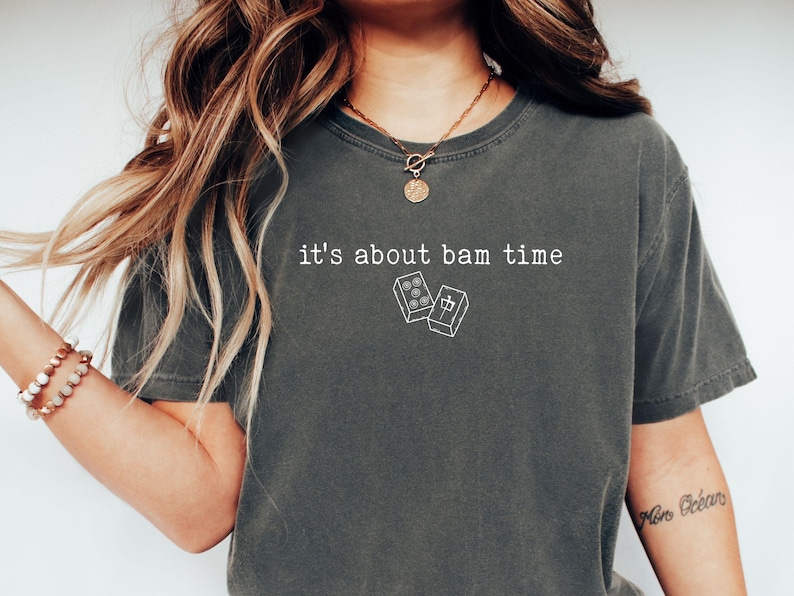 Pu&ograve; includere: T-shirt grigio scuro con la scritta bianca "it's about bam time" e una piccola grafica di domino. Una t-shirt casual e unisex.