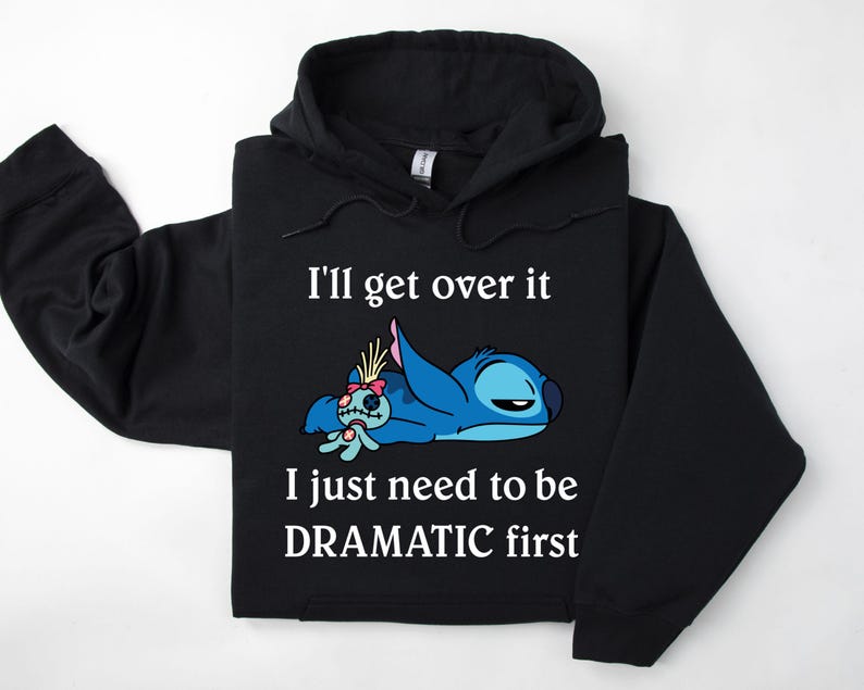 May include: Black hoodie featuring a blue Stitch character from Lilo & Stitch lying down with a small doll. The text on the hoodie reads "I'll get over it I just need to be DRAMATIC first."