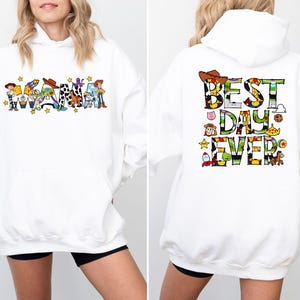 Puede incluir: Sudadera con capucha blanca con tem&aacute;tica de Toy Story. La parte delantera presenta la palabra "Mama" con personajes de Toy Story. La parte trasera presenta el texto "Best Day Ever" con personajes de Toy Story.