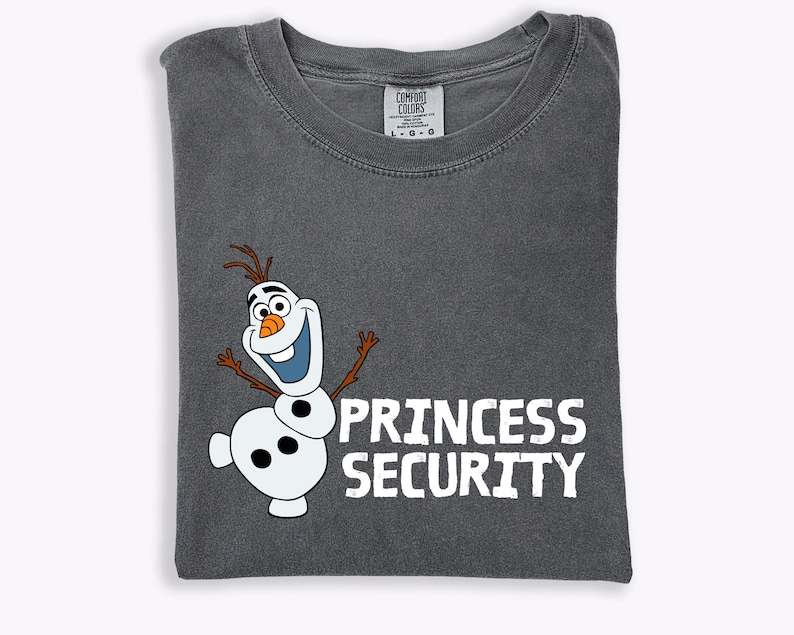 May include: Dark gray t-shirt featuring a cartoon snowman character with the text "PRINCESS SECURITY" in white. The snowman has a carrot nose, twig arms, and a smiling expression. The shirt is folded and has a Comfort Colors tag.