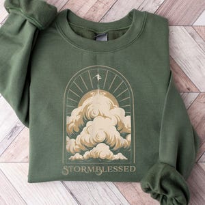 May include: A green sweatshirt with a graphic of a person standing on a cloud with the text "STORMBLESSED" below.