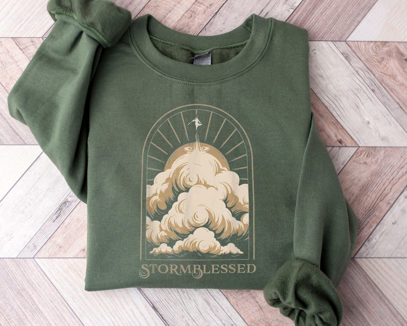 May include: A green sweatshirt with a graphic of a person standing on a cloud with the text "STORMBLESSED" below.