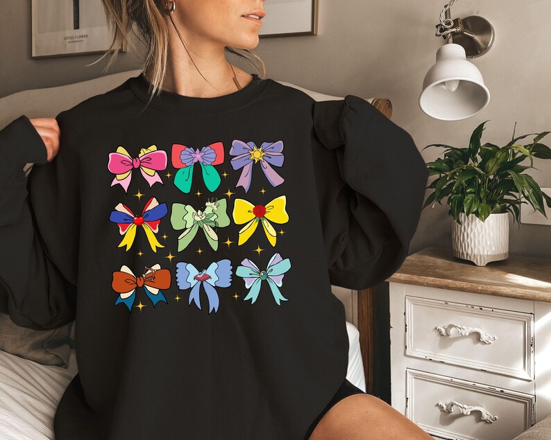 May include: Black sweatshirt with a colorful bow pattern. The bows are in various colors, including pink, blue, green, yellow, and purple. Each bow has a gold star in the center.