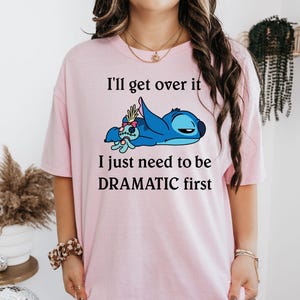 May include: Pink t-shirt featuring a blue Stitch character from Lilo & Stitch. The text on the shirt reads "I'll get over it I just need to be DRAMATIC first."