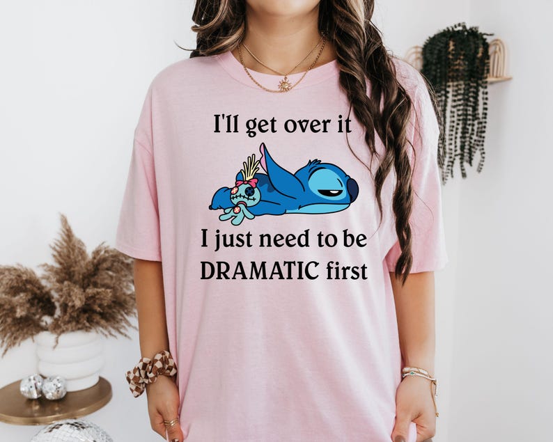May include: Pink t-shirt featuring a blue Stitch character from Lilo & Stitch. The text on the shirt reads "I'll get over it I just need to be DRAMATIC first."