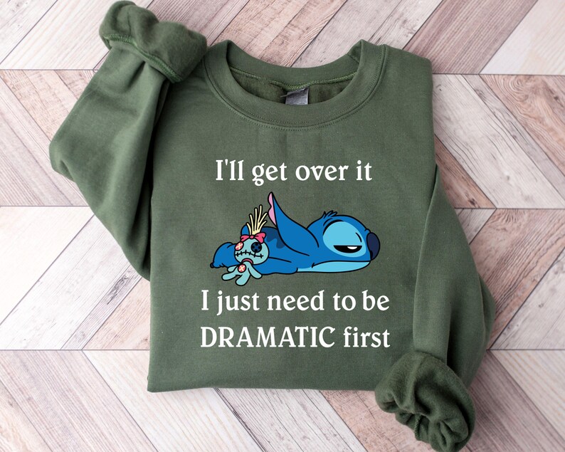 May include: Green sweatshirt featuring a blue Stitch character from Lilo & Stitch. The text on the sweatshirt reads "I'll get over it I just need to be DRAMATIC first."