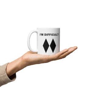 May include: White ceramic coffee mug with a black double diamond symbol and the text "I'm Difficult" printed on the side.