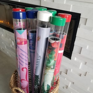 May include: A wicker basket holds several rolled-up posters in clear plastic tubes with colored caps. The posters feature various designs, including floral patterns, geometric shapes, and text. The caps are red, green, blue, and white.