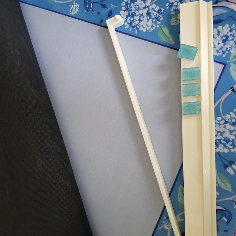 K&ouml;nnte beinhalten: Draufsicht auf einen cremefarbenen Papierhalter aus Kunststoff mit drei kleinen, quadratischen, blaugr&uuml;nen Haftnotizen. Ein langer, d&uuml;nner, cremefarbener Kunststoffstab ist &uuml;ber eine wei&szlig;e Oberfl&auml;che abgewinkelt. Der Hintergrund ist ein blaues Blumenmuster.