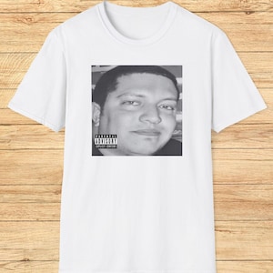 May include: White t-shirt with a black and white photo of a man's face on the front. The photo has a Parental Advisory label with the text "Explicit Content".