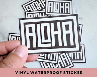 May include: A stack of black and white vinyl waterproof stickers with the word "ALOHA" printed in a bold, geometric font.