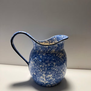 Puede incluir: Una jarra de cerámica azul y blanca con un diseño moteado. La jarra tiene un cuerpo redondeado y un asa curva.