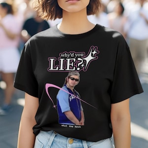May include: Black t-shirt featuring a pink graphic that reads "why'd you LIE?" with a pink star and a cartoon image of a person wearing a blue jacket and sunglasses. The text "what the heck" is below the graphic.