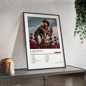 May include: Framed poster of the album art for "A For Arjan 2" by Arjan Dhillon. The image shows a man in a cowboy hat holding a gun, set against a backdrop of red roses. The poster includes a tracklist.
