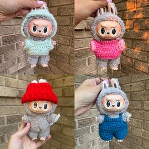 Puede incluir: Cuatro muñecos de peluche con capuchas de orejas de conejo y atuendos en varios colores: verde menta, rosa, rojo y peto azul. Cada muñeco tiene una cara redonda con ojos grandes y una boca pequeña.