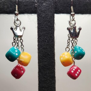 May include: A pair of silver dangle earrings with a crown charm and three dice charms in turquoise, yellow, and red.