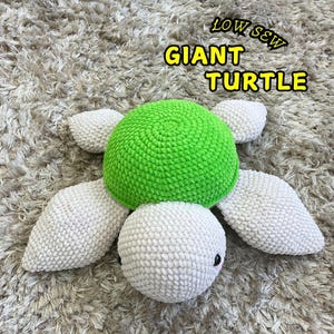 Puede incluir: Un juguete de tortuga de crochet con una concha verde y un cuerpo blanco. El juguete está hecho con hilo suave y tiene una cara amigable. El texto "LOW SEW GIANT TURTLE" está escrito encima del juguete.