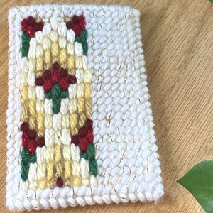May include: A white, rectangular, hand-stitched coaster with a floral design. The central pattern features a vertical arrangement of yellow and red flowers with green leaves. The border and accents include gold metallic thread.