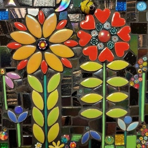 K&ouml;nnte beinhalten: Ein Mosaik-Kunstwerk, das eine Gartenszene mit drei Blumen darstellt. Die Blumen sind aus bunten Fliesen gefertigt und haben gr&uuml;ne Bl&auml;tter. Der Hintergrund ist ein dunkles Mosaik mit einem Stern und einem Halbmond.