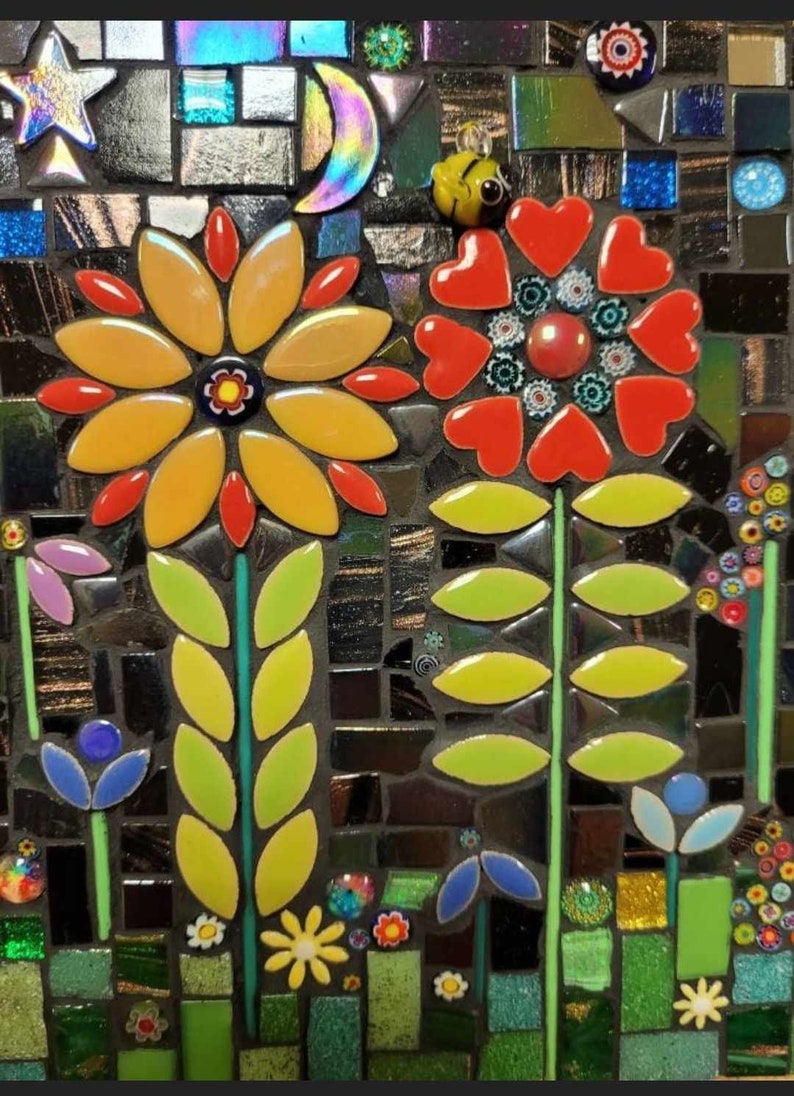 K&ouml;nnte beinhalten: Ein Mosaik-Kunstwerk, das eine Gartenszene mit drei Blumen darstellt. Die Blumen sind aus bunten Fliesen gefertigt und haben gr&uuml;ne Bl&auml;tter. Der Hintergrund ist ein dunkles Mosaik mit einem Stern und einem Halbmond.