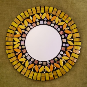 May include: A round mirror with a mosaic design. The mirror is surrounded by a ring of yellow, orange, and brown tiles. The tiles are arranged in a pattern of leaves and flowers.
