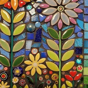 K&ouml;nnte beinhalten: Ein Mosaik-Kunstwerk mit einem floralen Design mit gelben, blauen, gr&uuml;nen und rosa Blumen. Die Blumen bestehen aus kleinen, bunten Fliesen und sind in einem symmetrischen Muster angeordnet.
