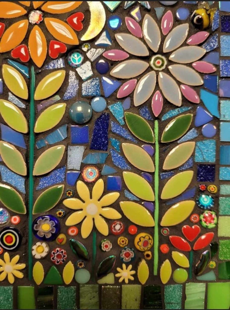 K&ouml;nnte beinhalten: Ein Mosaik-Kunstwerk mit einem floralen Design mit gelben, blauen, gr&uuml;nen und rosa Blumen. Die Blumen bestehen aus kleinen, bunten Fliesen und sind in einem symmetrischen Muster angeordnet.