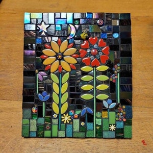 K&ouml;nnte beinhalten: Ein Mosaik-Kunstwerk, das eine Nachtgartenszene mit einer Mondsichel, einem Stern und drei Blumen mit gr&uuml;nen Bl&auml;ttern darstellt. Die Blumen sind gelb, rot und lila. Der Hintergrund ist schwarz mit schillernden Fliesen.