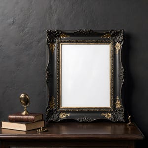 May include: A black ornate picture frame with gold accents stands on a dark wooden surface. A stack of books, a small brass mirror, and a decorative brass object are also on the surface. The background is a dark, textured wall.