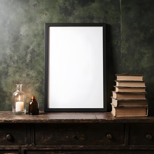May include: A black framed blank picture, a candle in a glass jar, a small brown bottle, and a stack of old books sit on a dark wooden dresser against a textured green wall.