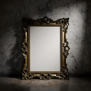 May include: Ornate gold-colored framed mirror with intricate carvings. The mirror has a blank white interior, set against a textured gray wall and floor. The frame is detailed with floral and scroll designs.