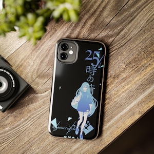 May include: Black phone case featuring a blue-haired anime-style character with the text "25-ji no Ghost" and "Nightcord at 25:00". The case has a silver frame and is on a wooden surface.