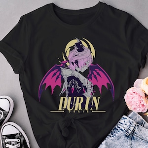 May include: Black t-shirt featuring a graphic of a character with pink hair, purple wings, and the word "DURIN" in gold lettering. The design is set against a yellow halo. The shirt is paired with jeans and black sneakers.