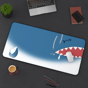 May include: A blue and white shark-themed mousepad with a red open mouth and a white computer mouse inside. The mousepad has a white border and a blue gradient.