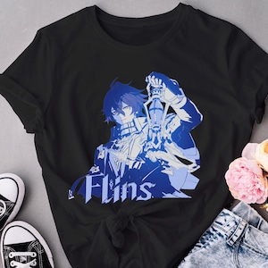 May include: Black t-shirt featuring a blue and white anime-style graphic of a character holding a lantern. The word "Flins" is printed in white below the graphic. The shirt is paired with denim jeans and black sneakers.