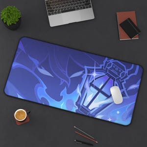 May include: A large blue and white mouse mat with a fantasy design of a glowing lantern and flames. A white computer mouse sits on the mat. The mat is on a dark surface with a laptop and other desk items.