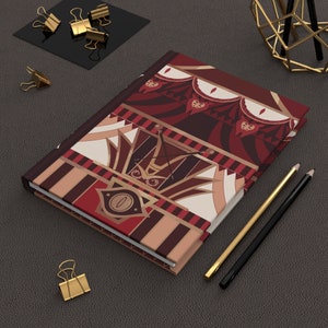 May include: A red, white and gold patterned journal with a whimsical design. The cover features a stylised eye with a crown and a circus tent motif.