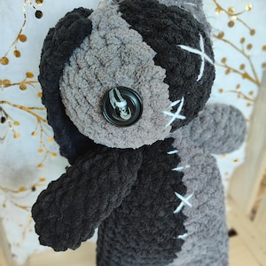 May include: A black and gray crocheted plush toy with a button eye and stitched details. The toy is stitched together with white thread.