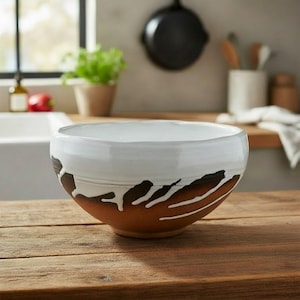 May include: A ceramic bowl with a white interior and a brown exterior. The bowl has a unique design with white and black accents. The bowl is on a wooden surface.