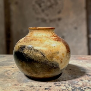 May include: A handmade ceramic vase with a rounded form and a slender neck. The vase displays a speckled, earthy colour scheme of tan, brown, and black, producing a natural, organic aesthetic. The vase is likely suitable for displaying flowers or as a decorative accent.