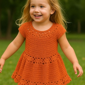 May include: A handmade, orange crochet dress for a young child. The dress features a detailed, openwork design around the neckline, waist, and hem. The short-sleeved dress is made of a soft, textured yarn and has a flared skirt.