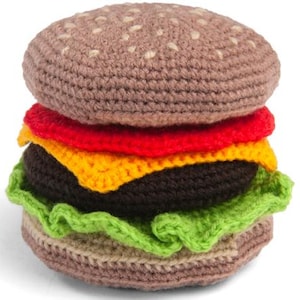 Puede incluir: Una hamburguesa hecha a mano con ganchillo, con pan marrón, tomate rojo, queso amarillo, una hamburguesa marrón oscura y lechuga verde. La hamburguesa es una escultura suave y juguetona, ideal para un juguete infantil o decoración de cocina.