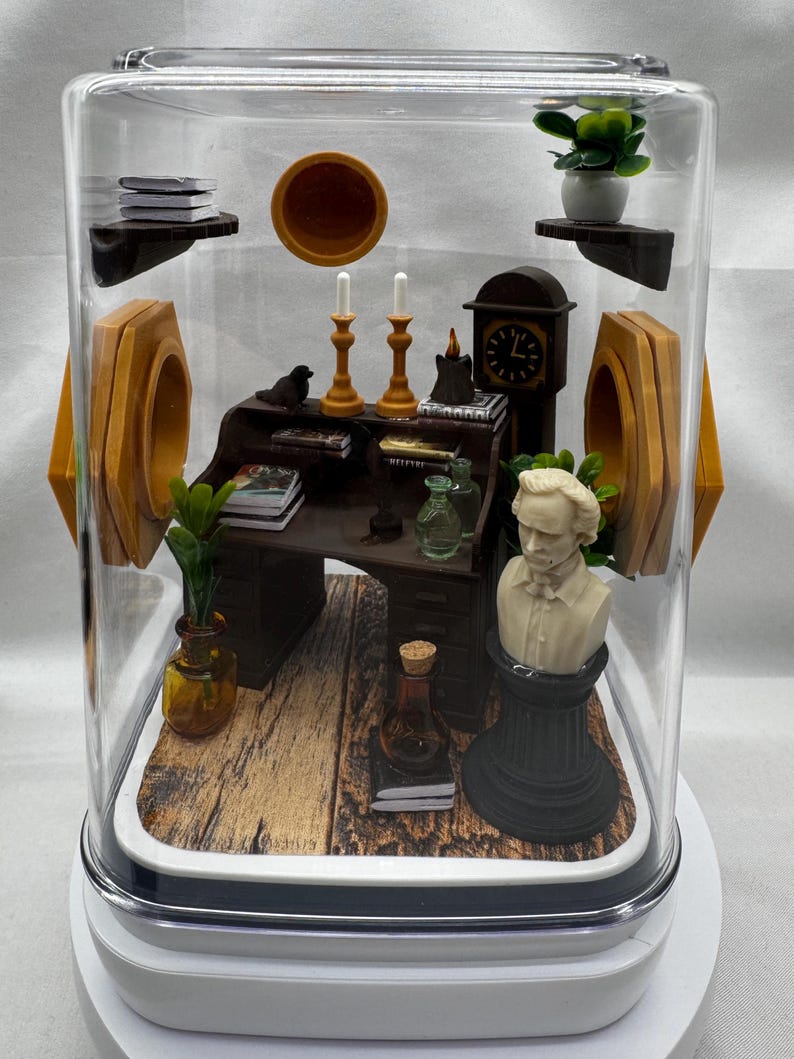 May include: Miniature diorama inside a clear display case. The scene includes a desk, bust, clock, candles, books, and plants. The diorama has a wooden floor and is enclosed in a clear, rectangular case with a white base.