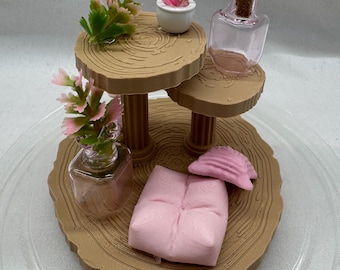 Peut inclure: Un diorama miniature avec une structure en bois à plusieurs niveaux, des plantes artificielles et de petits objets décoratifs. La scène comprend un petit coussin rose, un coquillage et une bouteille en verre avec un bouchon.