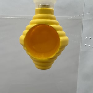 May include: A yellow plastic beehive-shaped birdhouse with a round opening. The birdhouse is hanging from a clear plastic string.