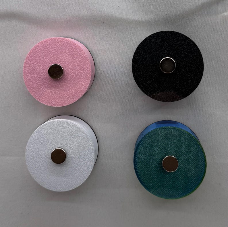 Puede incluir: Cuatro imanes redondos en rosa, negro, blanco y verde azulado. Cada im&aacute;n tiene un peque&ntilde;o centro met&aacute;lico circular. Los imanes est&aacute;n dispuestos en un patr&oacute;n cuadrado sobre un fondo blanco. Los imanes son probablemente para un refrigerador o una pizarra.